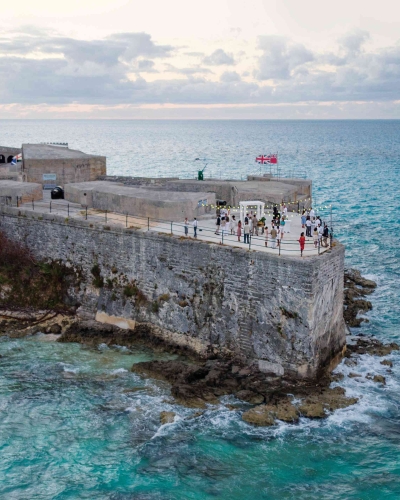 A group of people are standing in an old scenic fort by the water.