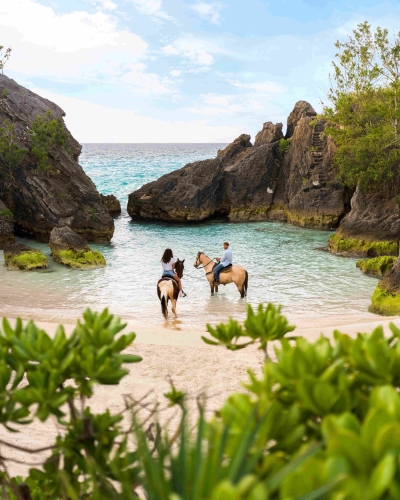 A couple are on horses in a secluded beach.