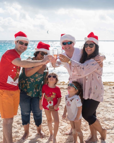 A family is cheering while on the beach in Christmas gear.