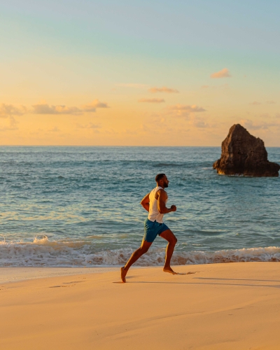 A man is running at sunrise on a empty beach with calm ocean waters in the background.