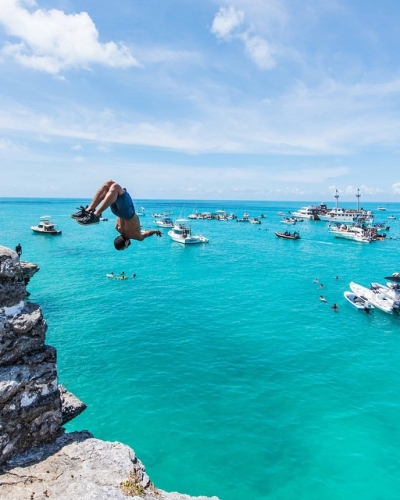 A person doing a backflip off a rock into the sparkling blue waters of Bermuda