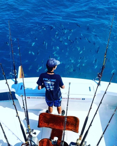 A man on a fishing boat watching a school of fish in the water