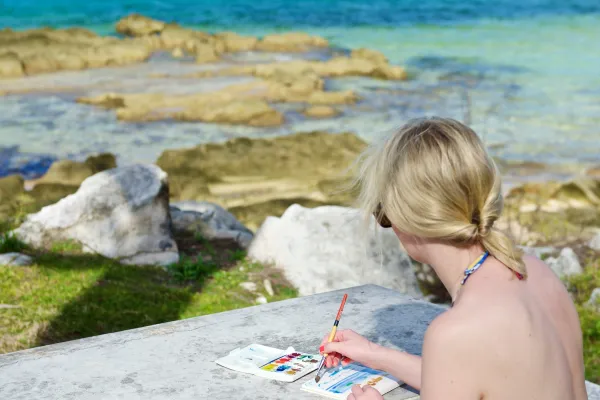 A woman sketches at an outdoor table by the oceanside in Bermuda