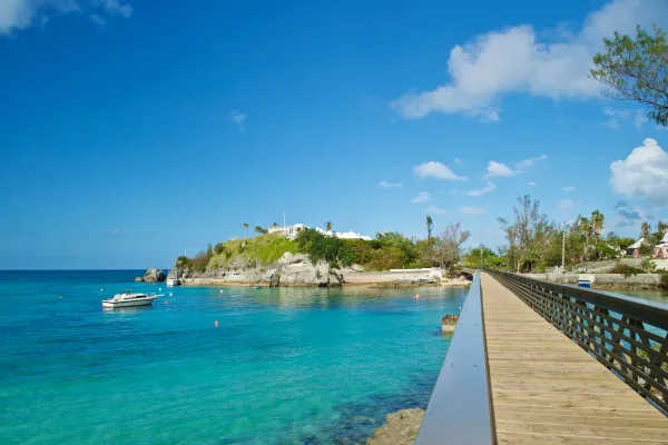 A bridge extending over blue waters in Bermuda, next to a hill with a fortification on it
