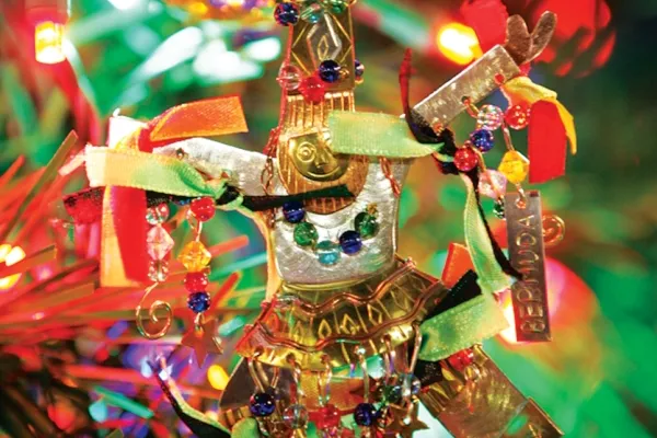 A Gombey christmas ornament hanging on an illuminated Christmas tree