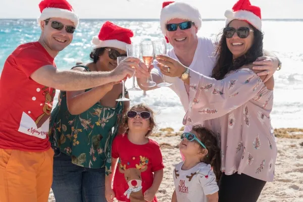 A family in santa hats clinking their drinking glasses on a beach in Bermuda