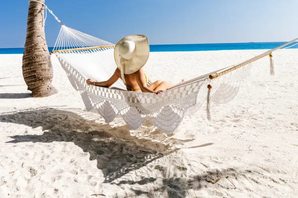 A woman in a sun hat relaxes in a hammock on a white sandy Bermuda beach 