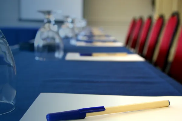 A conference table with a blue table cloth, with place settings including pens, notepads and water glasses
