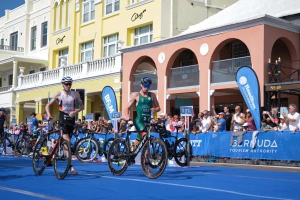 Cyclists participating in a triathalon wheel their bicycles through a cityscape in Bermuda