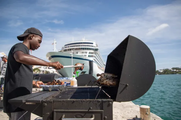 A person grilling on a dock next to a cruise ship,  in Bermuda