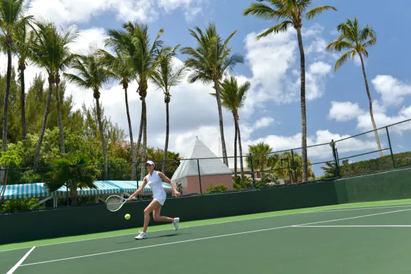 A woman returns a shot at a Bermuda tennis court