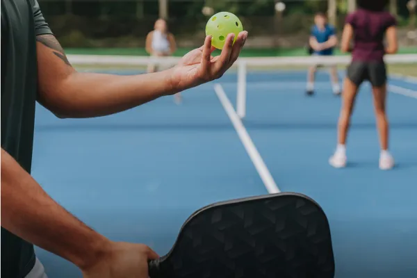 A man prepares a pickleball serve on a Bermuda court