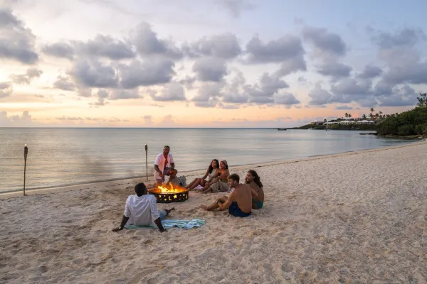 Friends enjoying a bonfire on a Bermuda beach at dusk