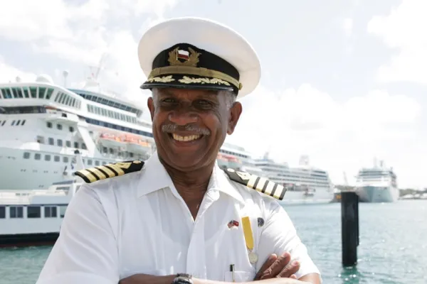 A Bermuda boat pilot standing on a dock in front of a boat with his arms crossed, smiling