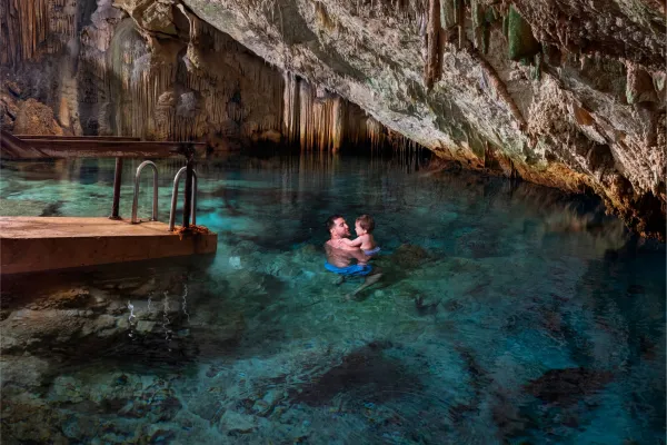 A father holds his child in his arms in the water of the Crystal Caves of Bermuda
