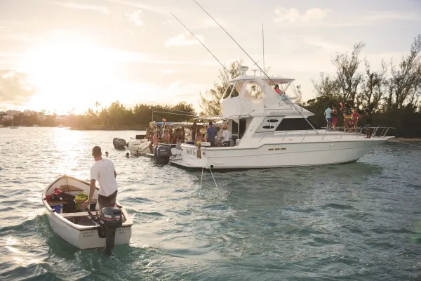 A man drives a small boat next to a larger one at sunset in Bermuda