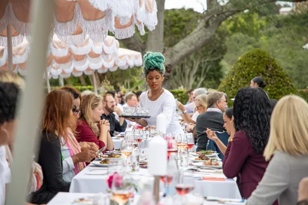 A woman serves a table of patrons their food at an outdoor dining terrace in Bermuda