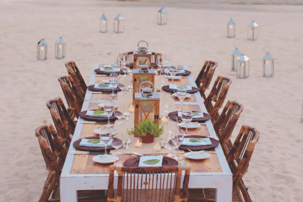 A banquet table set up for a wedding dinner, on the beach, surrounded by lanterns