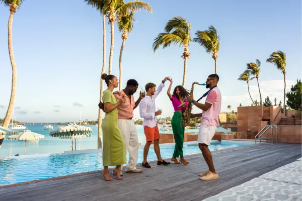 Friends laughing and dancing as a saxophone player performs poolside in Bermuda