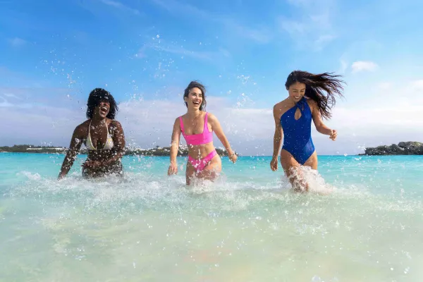Three women are splashing in the water on a beach in Bermuda
