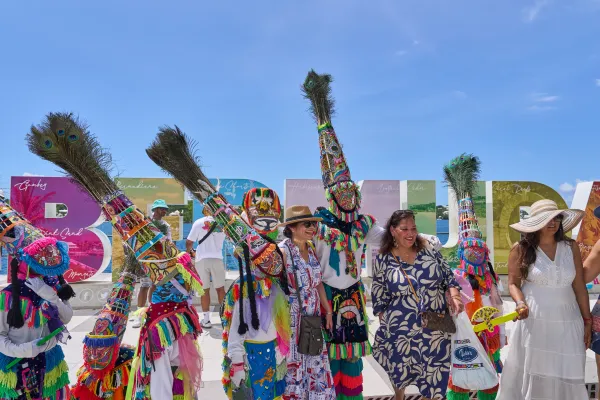 Women pose with Gombeys in front of a colourful Bermuda sign