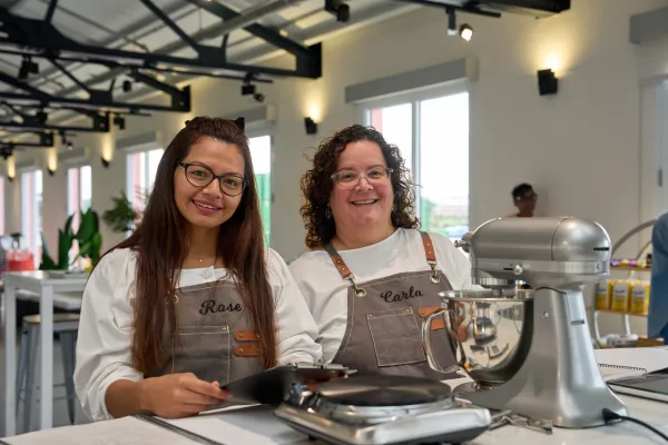 Two bakers in aprons participating in the Baker's retreat in Bermuda smiling standing at work station with a stand mixer