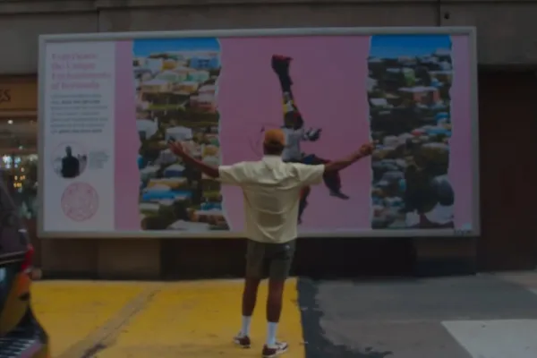 A man standing with his arms outstretched in front of a pink Bermuda advertisement