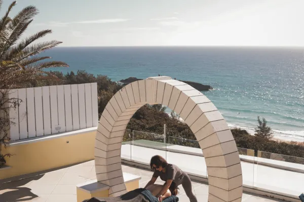 A person is getting a massage under a moongate by the sea. 