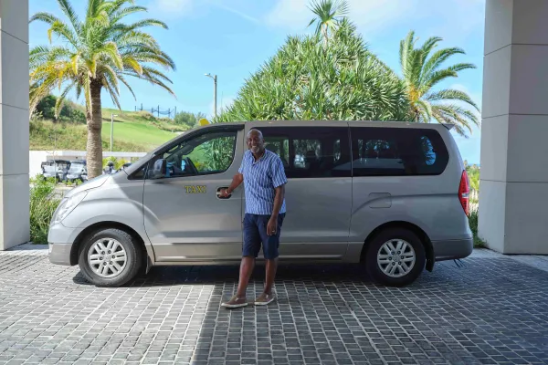 A taxi driver is standing holding the door to the passenger seat.