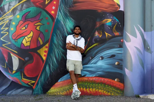 Dion is posing by a mural.