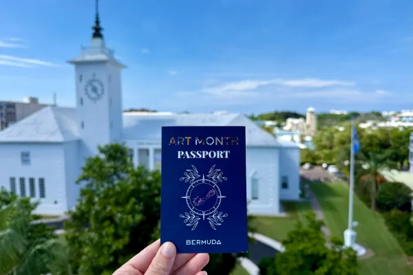 A close up of a Bermuda art month passport with a building blurred in the background