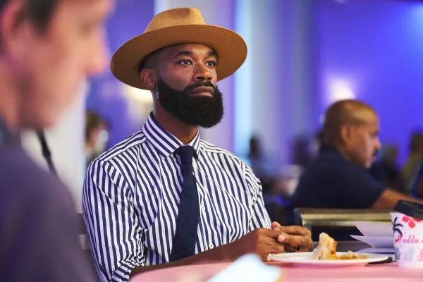 A man in a striped shirt is listening in a crowd. 