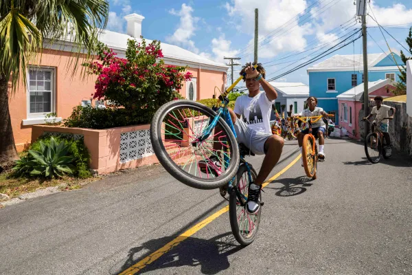 A group of boys are riding bikes in the streets with gombeys and colour buildings are behind them.