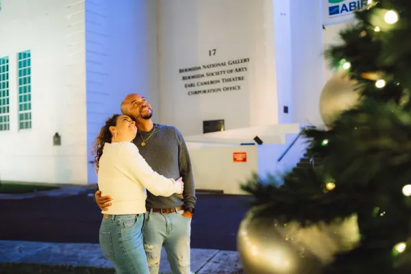 A couple are posing by a Christmas tree.