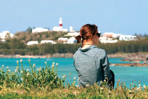 A woman facing away from the camera with the view of Cooper's Island lighthouse in the foreground.