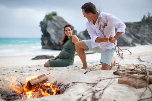 A woman and a man are sitting on the beach by a bonfire. 