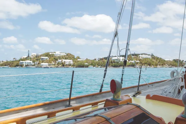 Exterior view of a sail boat with island houses and greenery in the background.