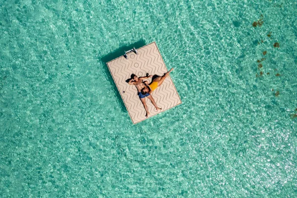 A couple is cuddling while floating on a dock surrounded by turquoise waters.