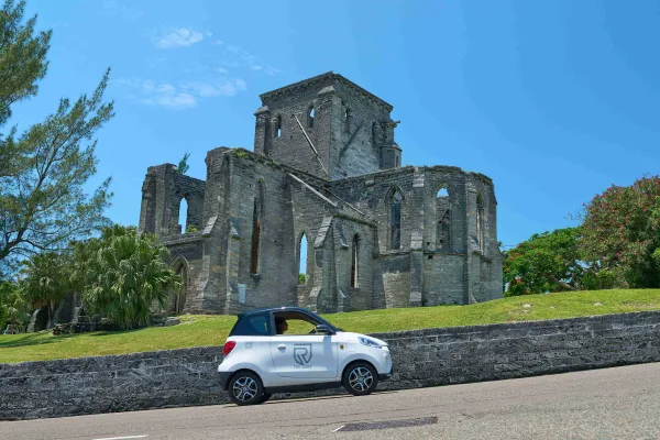 A person is driving an electric microcar by a scenic building.