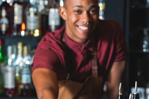 A bartender is smiling at the camera while passing a drink over.