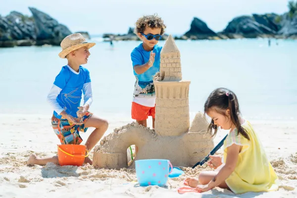 A group of kids are playing in the sand at the Hamilton Princess Beach Club