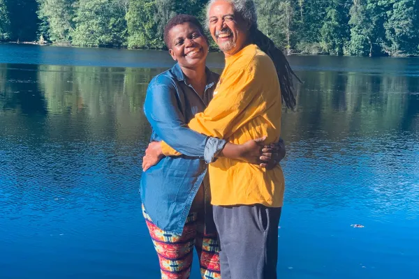 A couple are standing on a dock smiling at the camera.