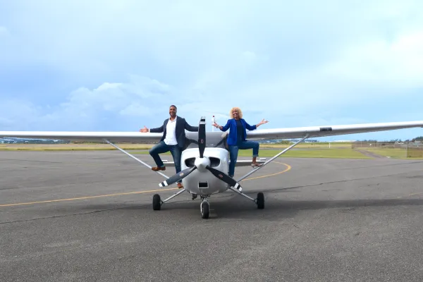 Two pilots are standing on a propeller plane.