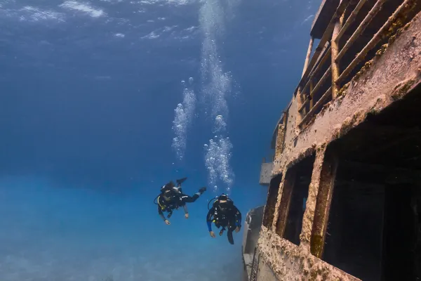 People swimming underwater by a shipwreck.