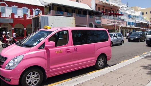 A pink taxi van parked on the side of a road.
