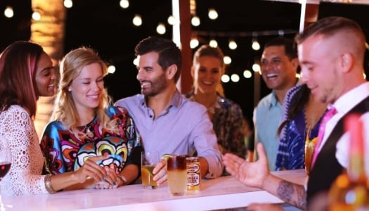 Bar scene with the focus on two girls and one guy laughing with drinks