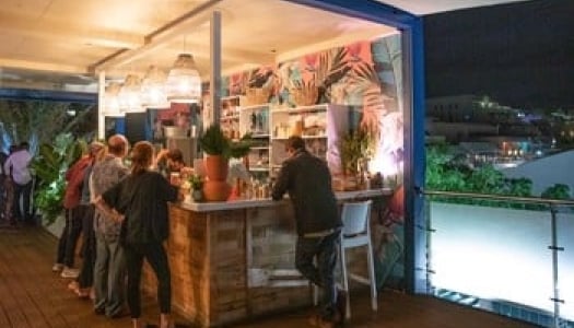 A bar in the nighttime with colorful walls and people standing in front of a bartender 