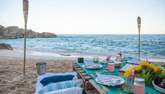 A luxe picnic table set up on the beach at dusk.