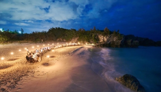 Beach at night with a large table sitting people and lights surrounding them