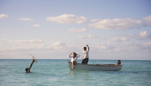 A man fishing for spiny lobster in Bermuda, a couple is cheering from the boat.